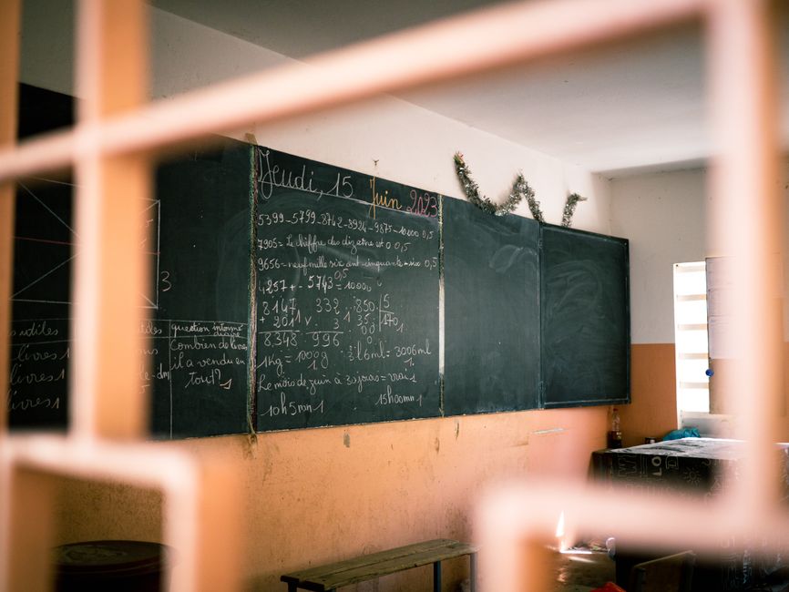 scolariser ses enfants à Annecy – A classroom with a blackboard displaying mathematical equations in French, seen through a window.